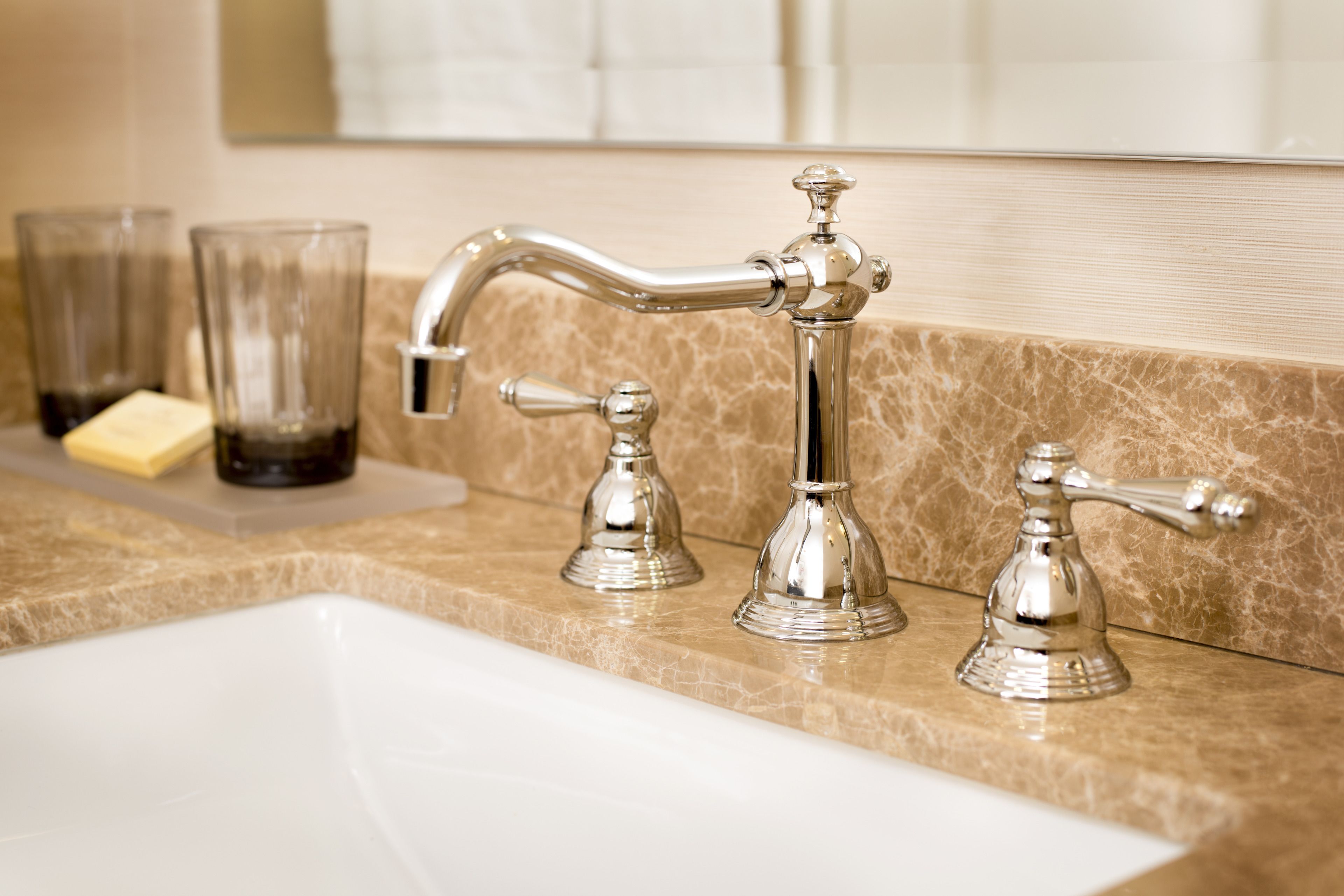 A bathroom with a white sink, two chrome faucets, and a marble countertop.