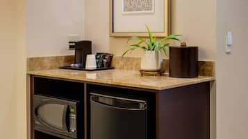 A compact kitchenette with a microwave, refrigerator, coffee maker, and a small potted plant.