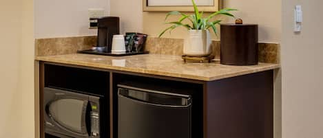 A compact kitchenette with a microwave, refrigerator, coffee maker, and a small potted plant.