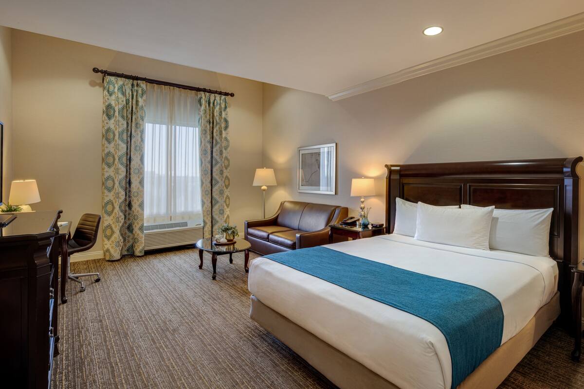 Ein Hotelzimmer mit einem großen Bett, einem Schreibtisch mit Computer, einem Stuhl und einem kleinen Tisch.