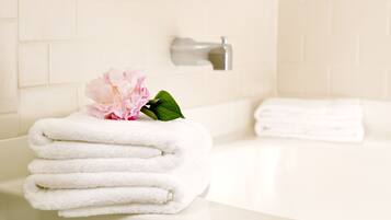 Une salle de bain avec une baignoire blanche, des piles de serviettes blanches et une fleur rose posée sur le bord.
