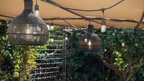 Een buitenpatio met tafels, stoelen, lichtjes en beplanting.