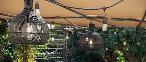Ein Außenbereich mit Terrasse, Tischen, Stühlen, Lichterketten und Bepflanzung.