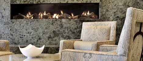 A modern living room with a stone wall, a fireplace, patterned furniture, and a glass table.