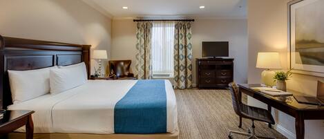 A hotel room with a large bed, a desk with a chair, a television, and a window with curtains.