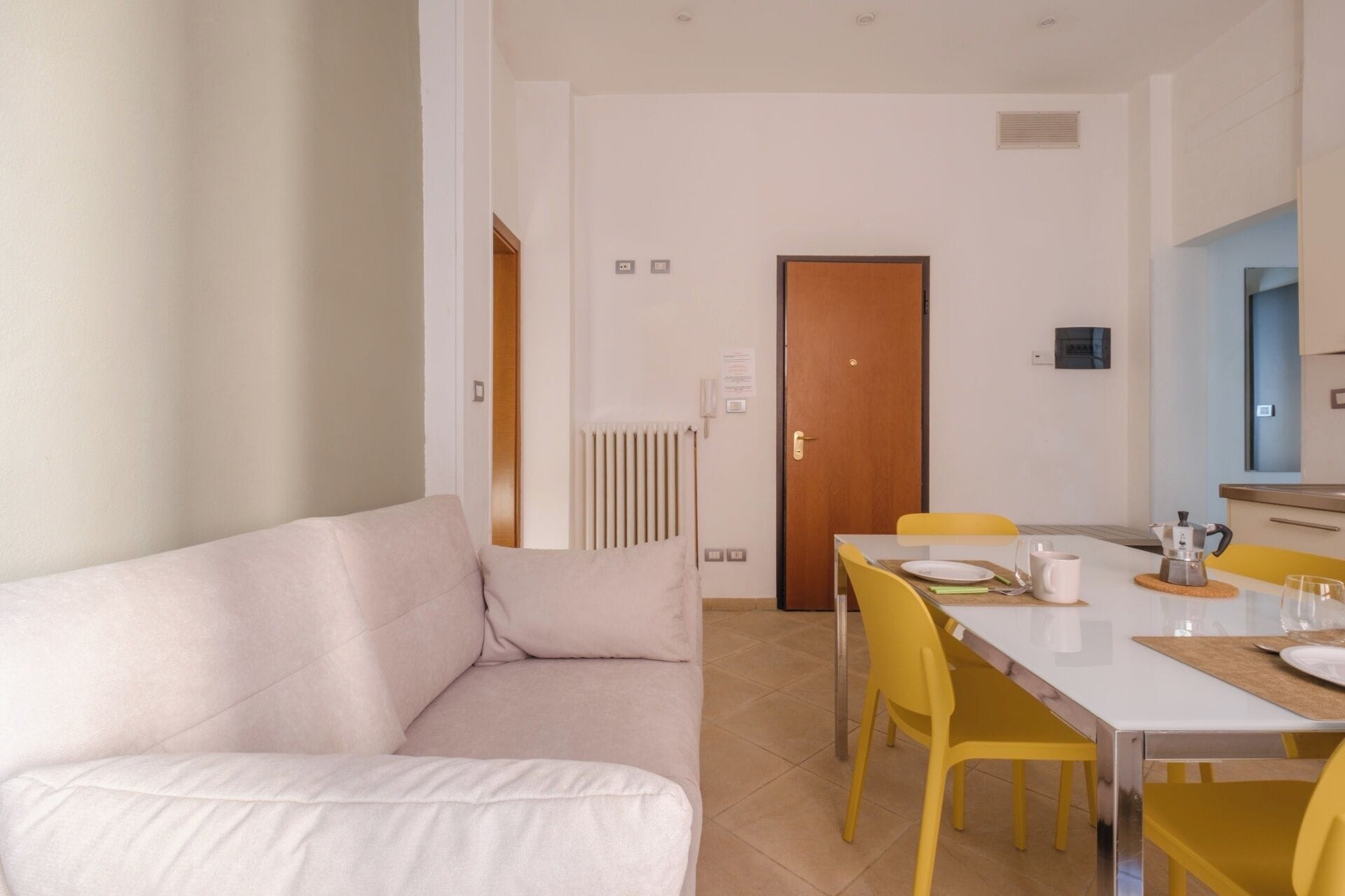 Una sala moderna con un sofá blanco, una mesa de comedor con sillas amarillas y una puerta de madera.