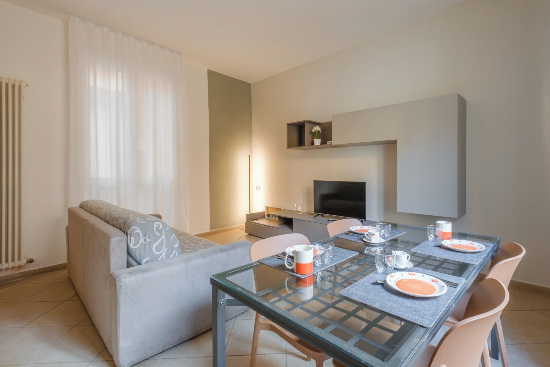 A modern living room with a glass dining table set for four, a sofa, a TV, and a fireplace.