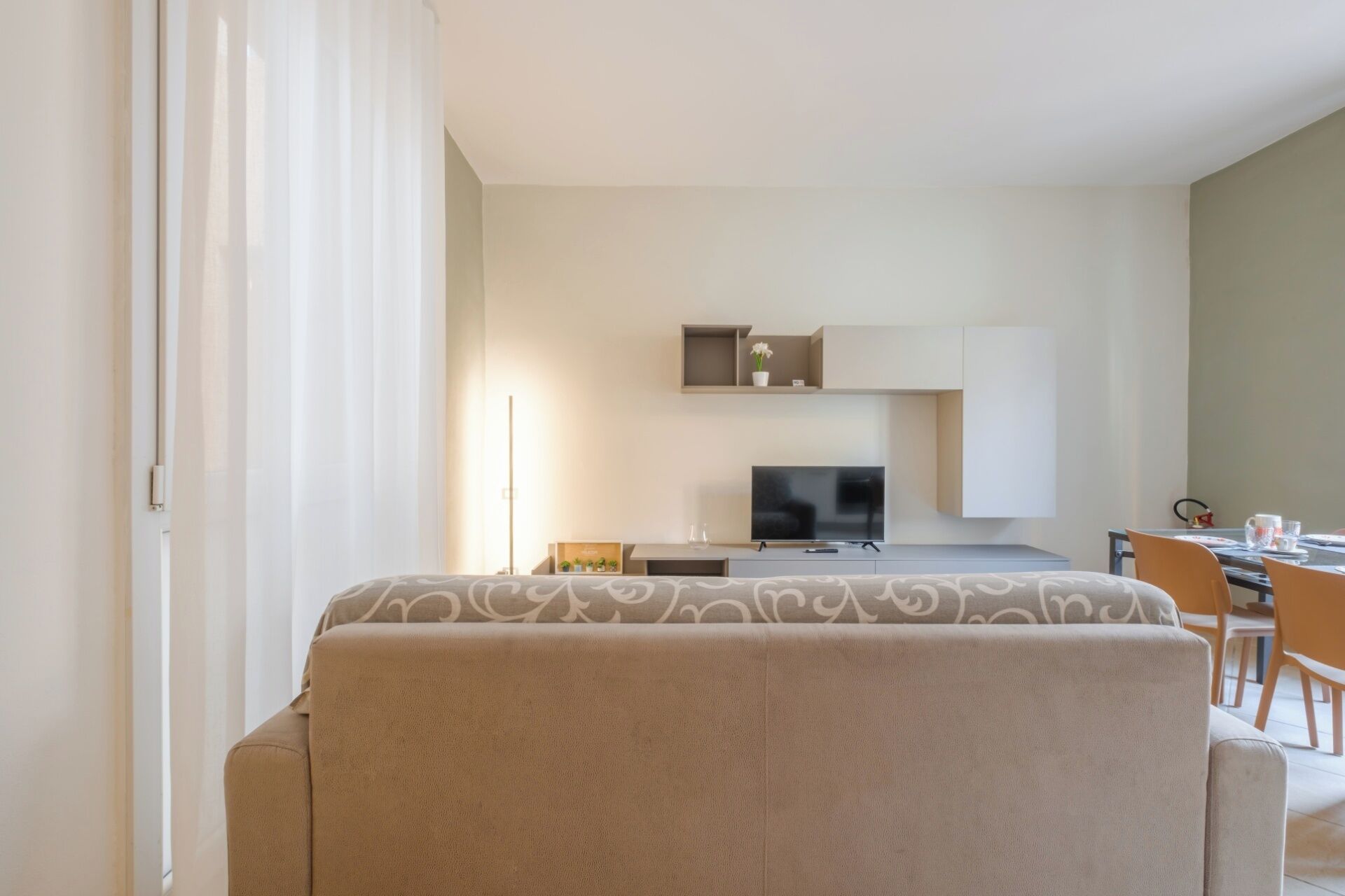 Une chambre d’hôtel moderne et minimaliste, dotée d’un canapé, d’un téléviseur à écran plat, d’un petit coin cuisine et d’une table à manger.