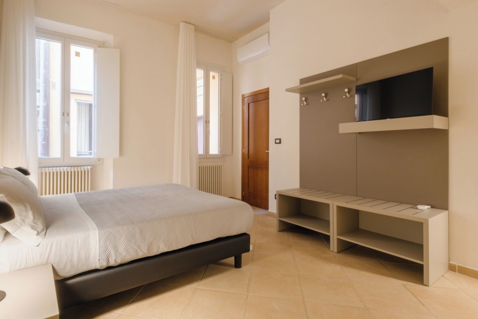 Quarto com cama, prateleira para TV embutida e radiador.