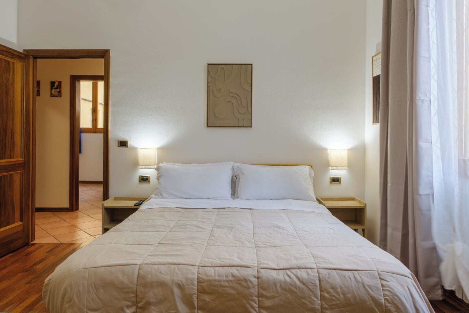 A neatly made bed with a quilted cover, two bedside lamps, and a wall-mounted artwork.