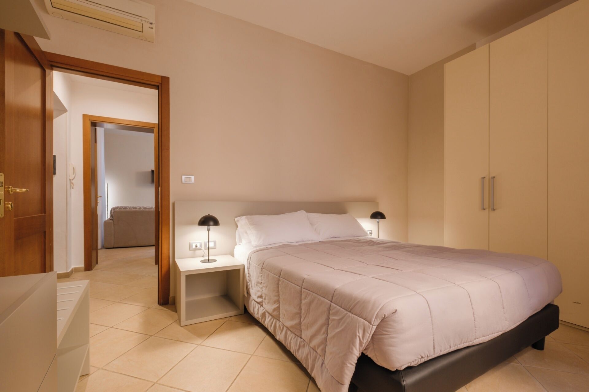 Une chambre à coucher comprenant un lit, des tables de chevet, une armoire et une porte donnant sur une autre pièce.