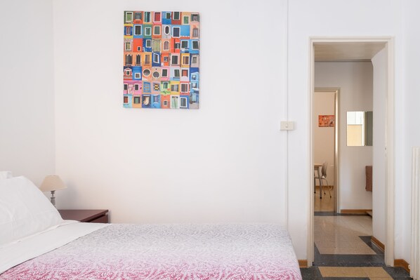 A hotel room with a bed, a nightstand, a lamp, and a colorful artwork on the wall. - Residenza Ariosto (Bologna)