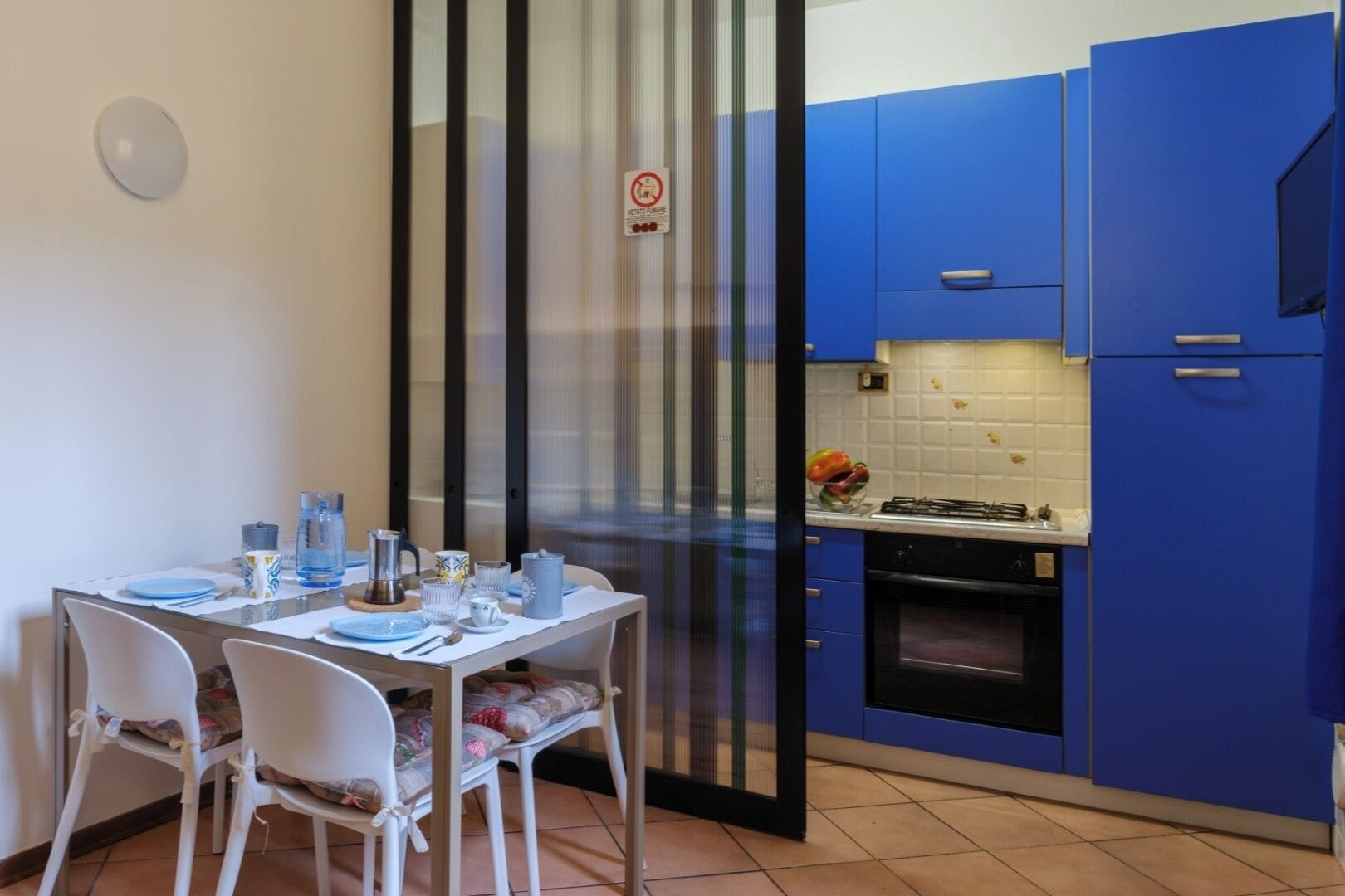 A compact kitchen with blue cabinets, a stove, and a dining area with a table set for two.