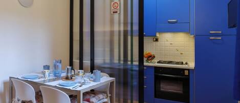 A compact kitchen with blue cabinets, a stove, and a dining area with a table set for two.