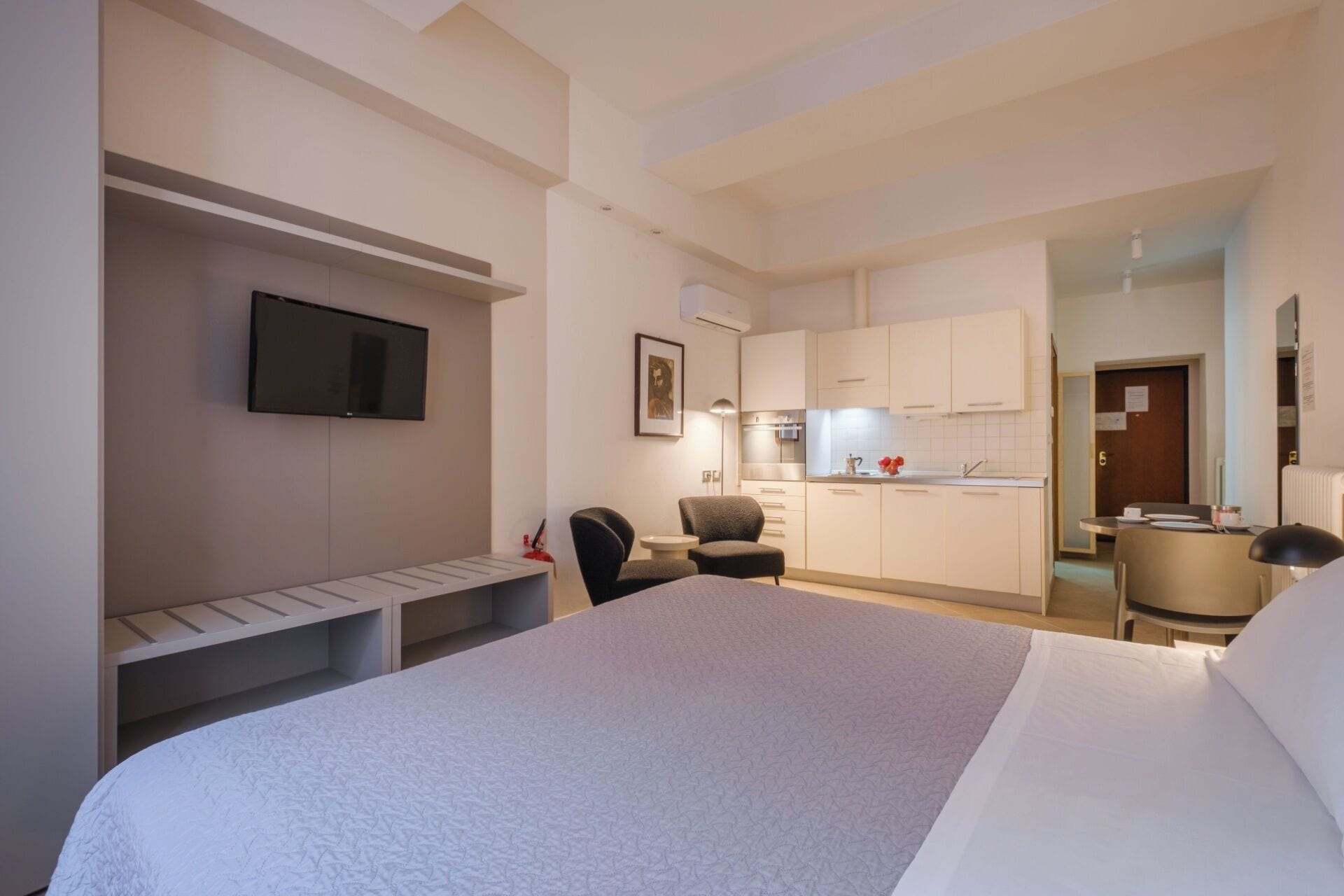 A hotel room with a bed, a desk, a chair, a TV, a kitchenette, and a bathroom.