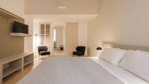 Un dormitorio con una cama grande, dos sillones, un televisor en la pared y un armario.