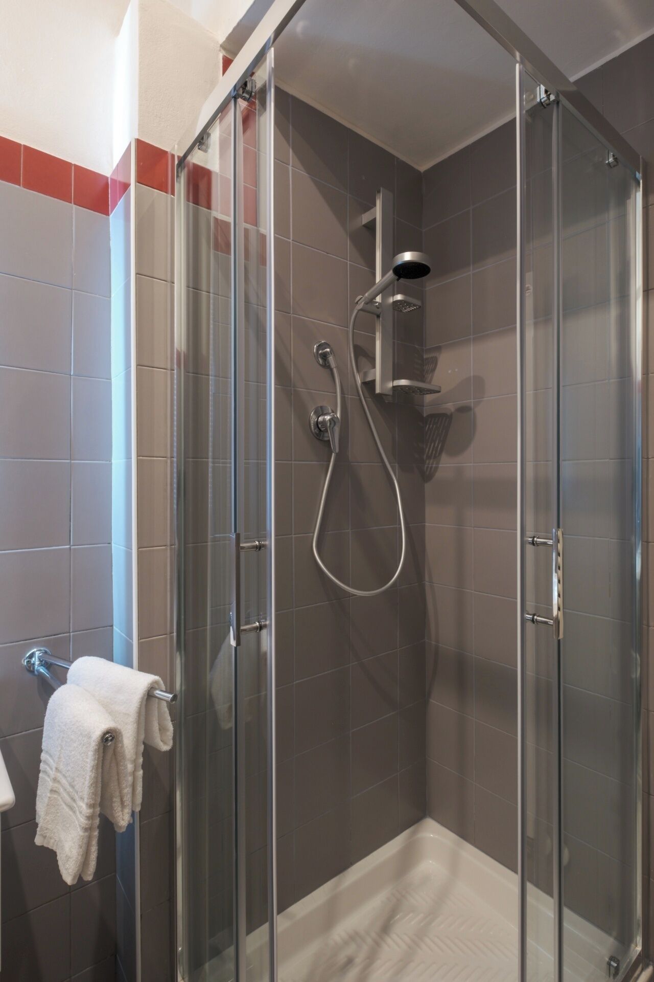 A glass-enclosed shower with a handheld showerhead and a wall-mounted faucet.