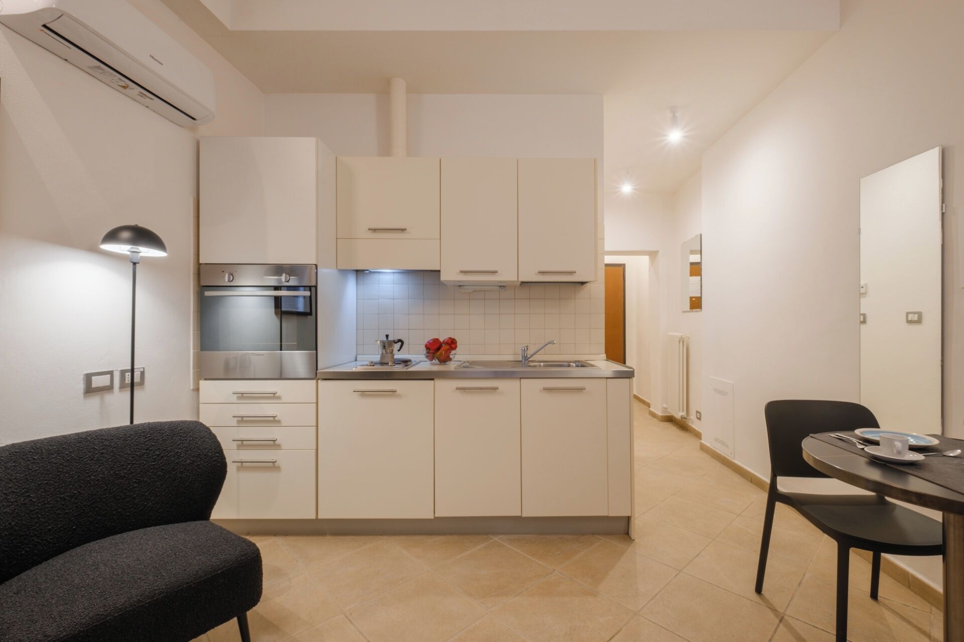 Een moderne keuken met witte kastjes, een ingebouwde oven en een spoelbak. Er is een eethoek met een tafel en stoelen.