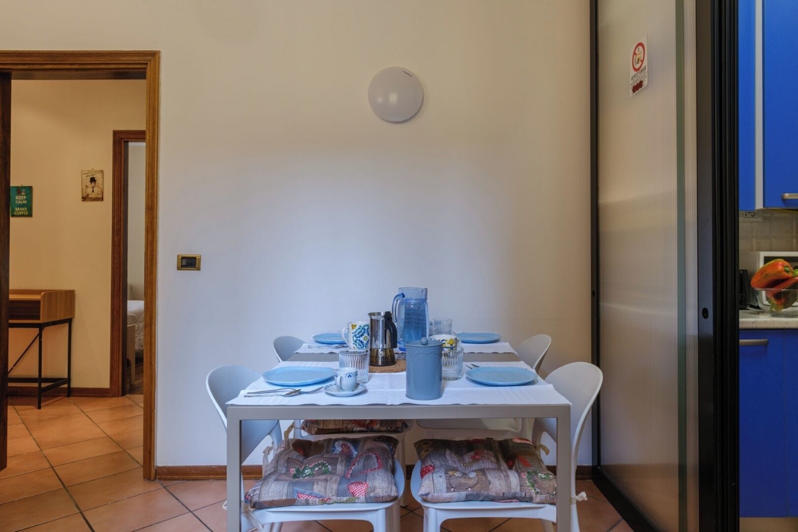 Een eethoek met een tafel voor vier personen, witte stoelen en een blauwe tafelkleed.