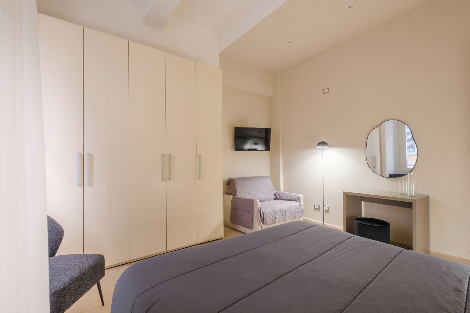 Ein Schlafzimmer mit Bett, Stuhl, Schreibtisch, Spiegel und Kleiderschrank.