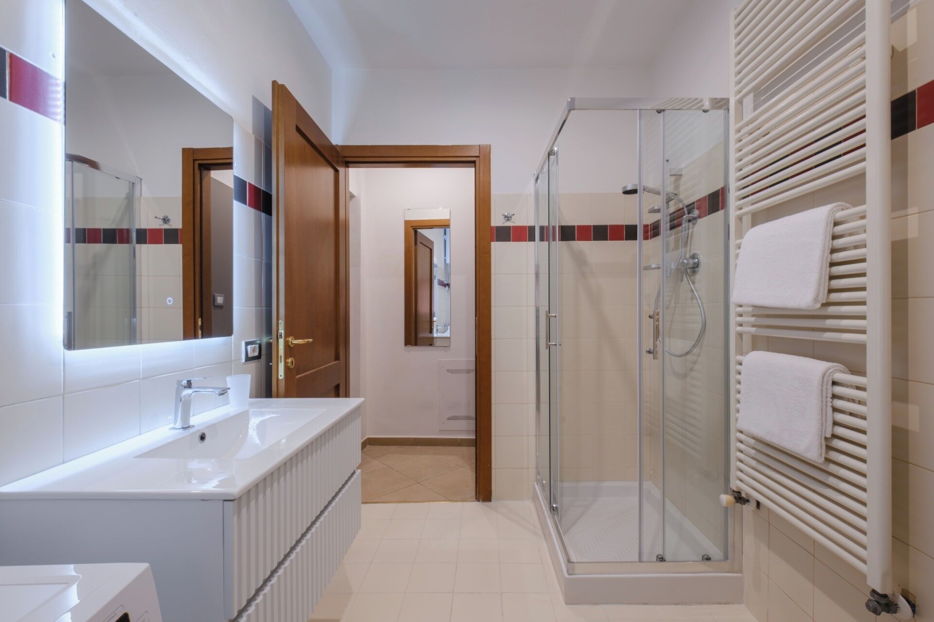 A modern bathroom with a glass shower enclosure, a large mirror, and a white sink.