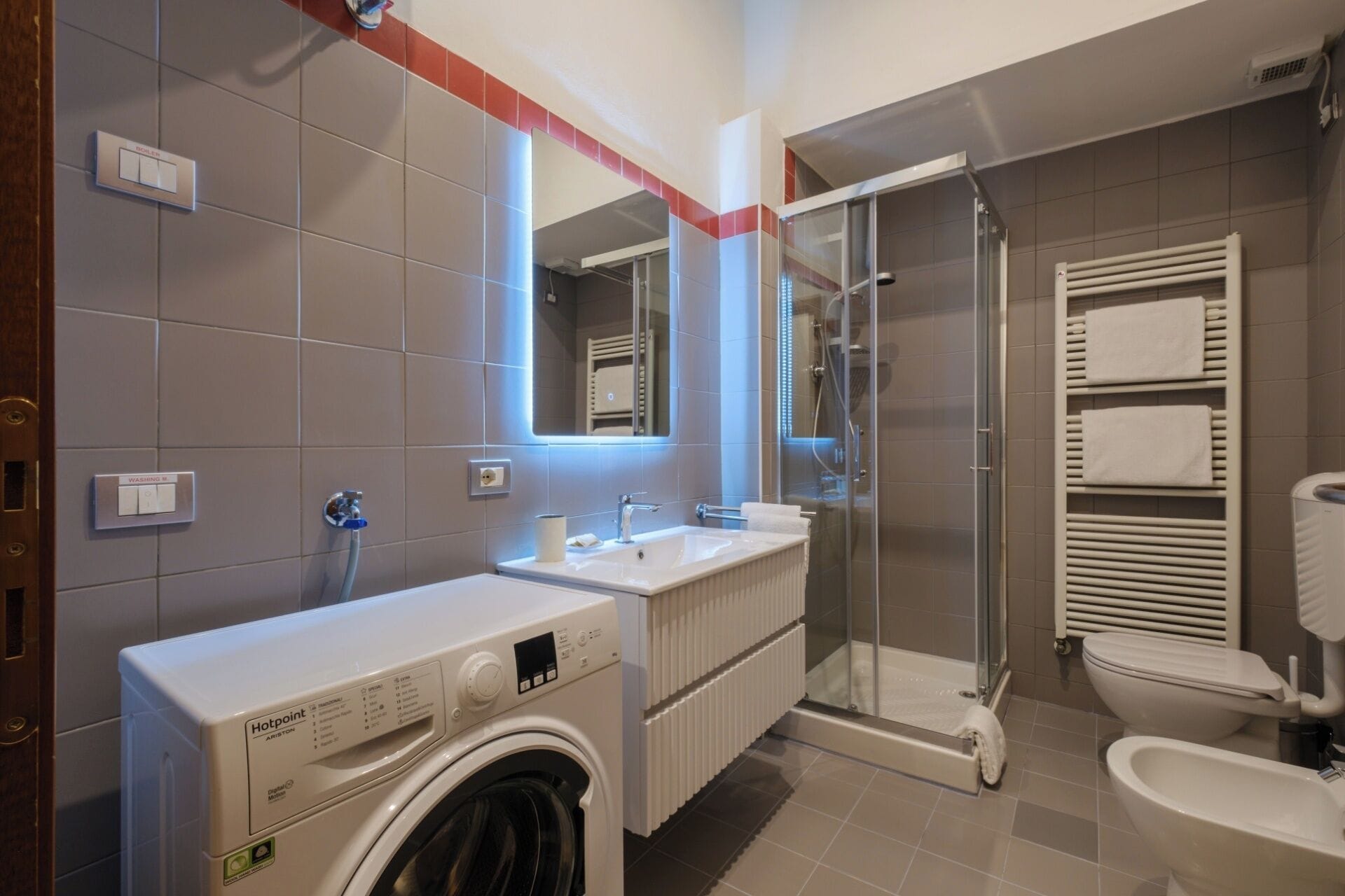 A modern bathroom with a washing machine, a sink, a glass shower enclosure, and a toilet.