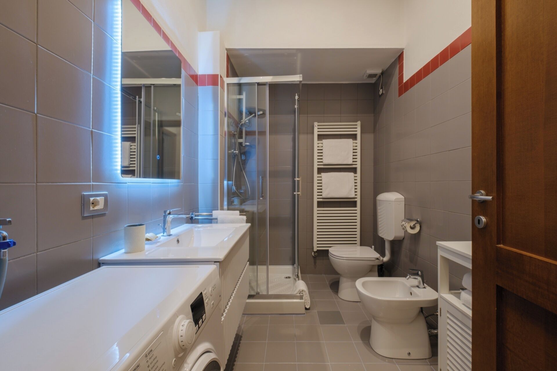 A modern bathroom with a built-in washing machine, a shower, a toilet, and a bidet.