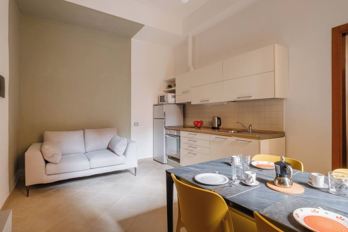 A compact living space with a sofa, a dining table set for two, and a kitchen area with cabinets and a microwave.