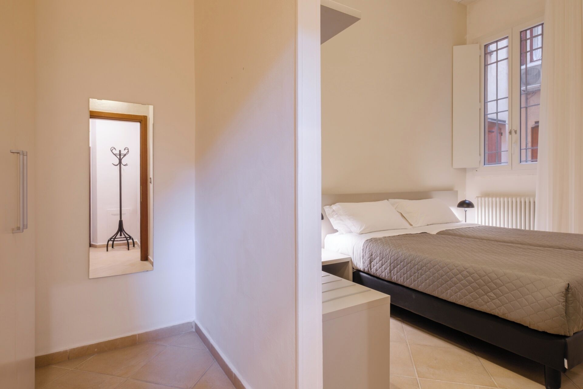Une chambre à coucher avec un lit, un radiateur et une fenêtre donnant sur des immeubles.