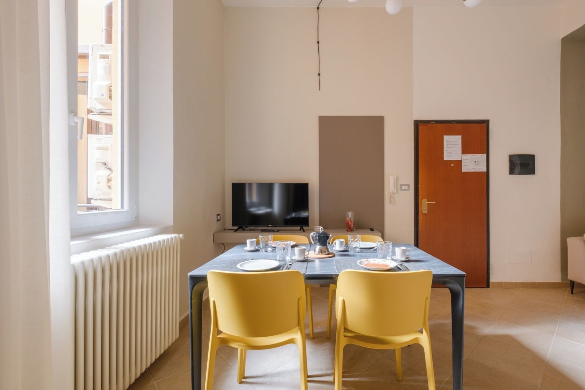 A dining area with a table set for four, a television, and a door with a notice.