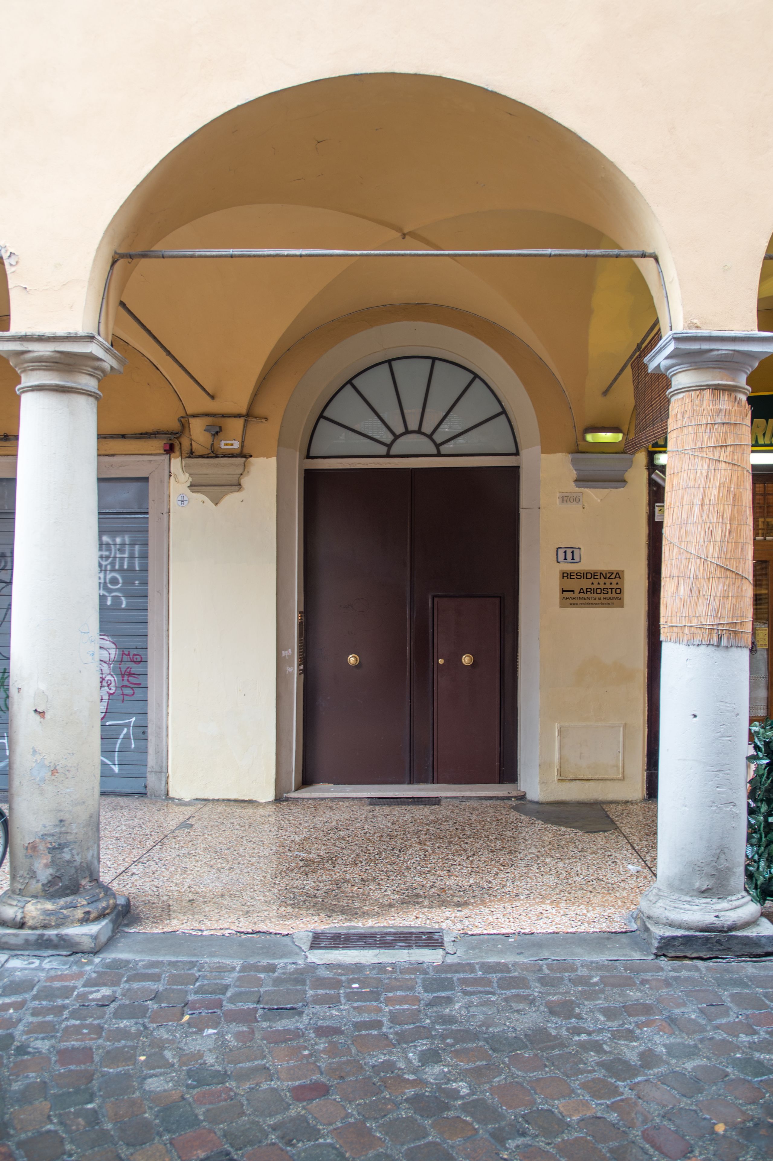 A building entrance with a dark wooden door, an arched overhang, and a sign indicating the address and name.