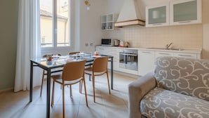 Una cocina compacta con comedor, un sofá y un ventanal con cortinas.