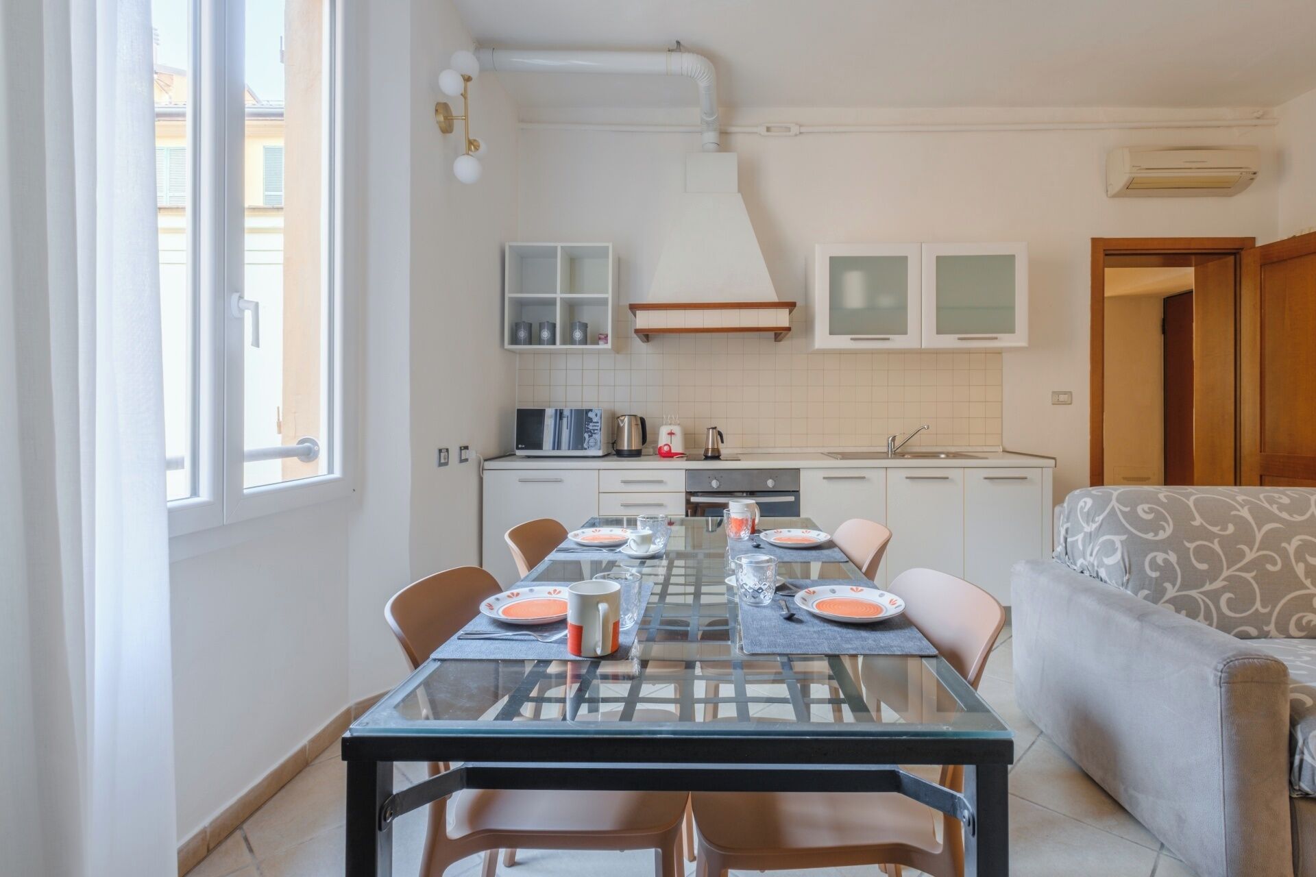 A compact kitchen with a dining table set for four, a sofa, and a window with curtains.