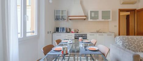 A compact kitchen with a dining table set for four, a sofa, and a window with curtains.