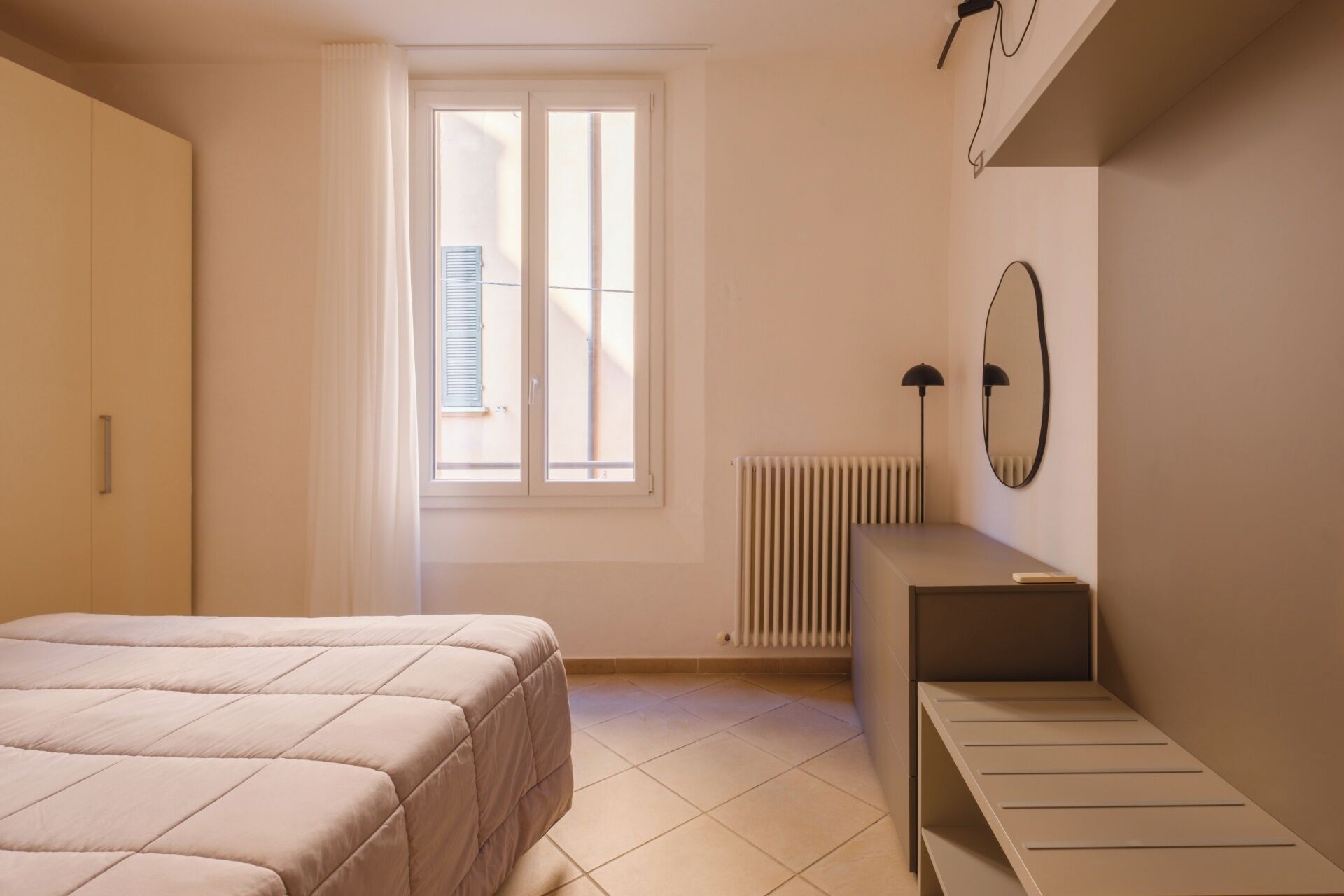 A bedroom with a bed, a radiator, a desk, and a window with blinds.