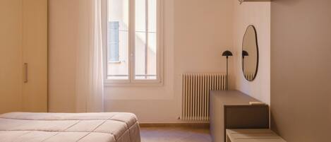 Een slaapkamer met een bed, een radiator, een bureau en een raam met zonwering.
