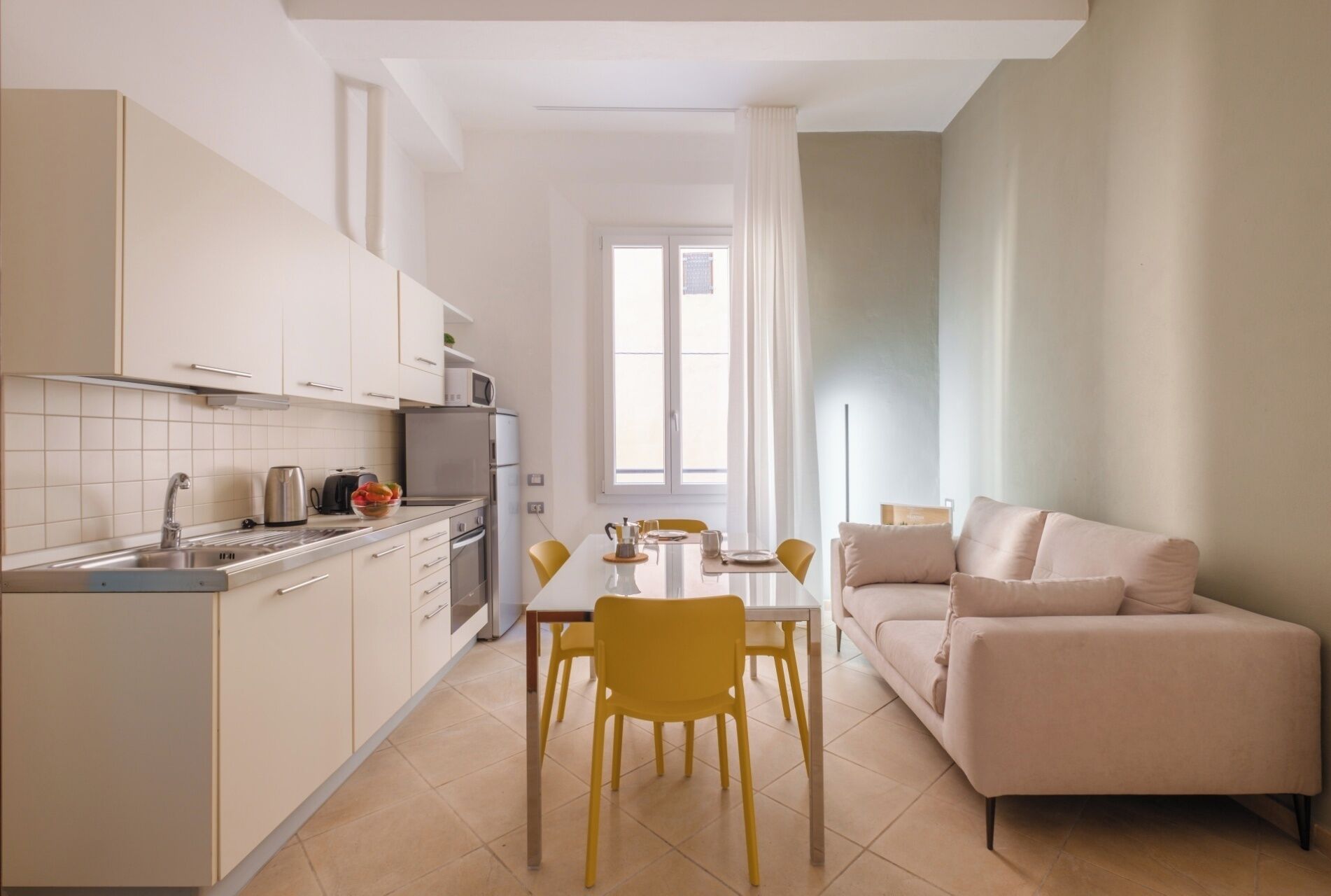A modern kitchen with white cabinets, a dining table with yellow chairs, and a beige sofa.