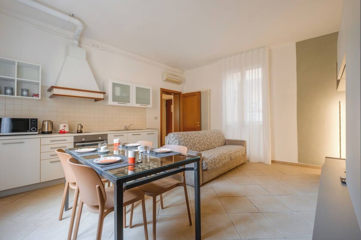 A compact kitchen with a dining area, a sofa, and a window with curtains.