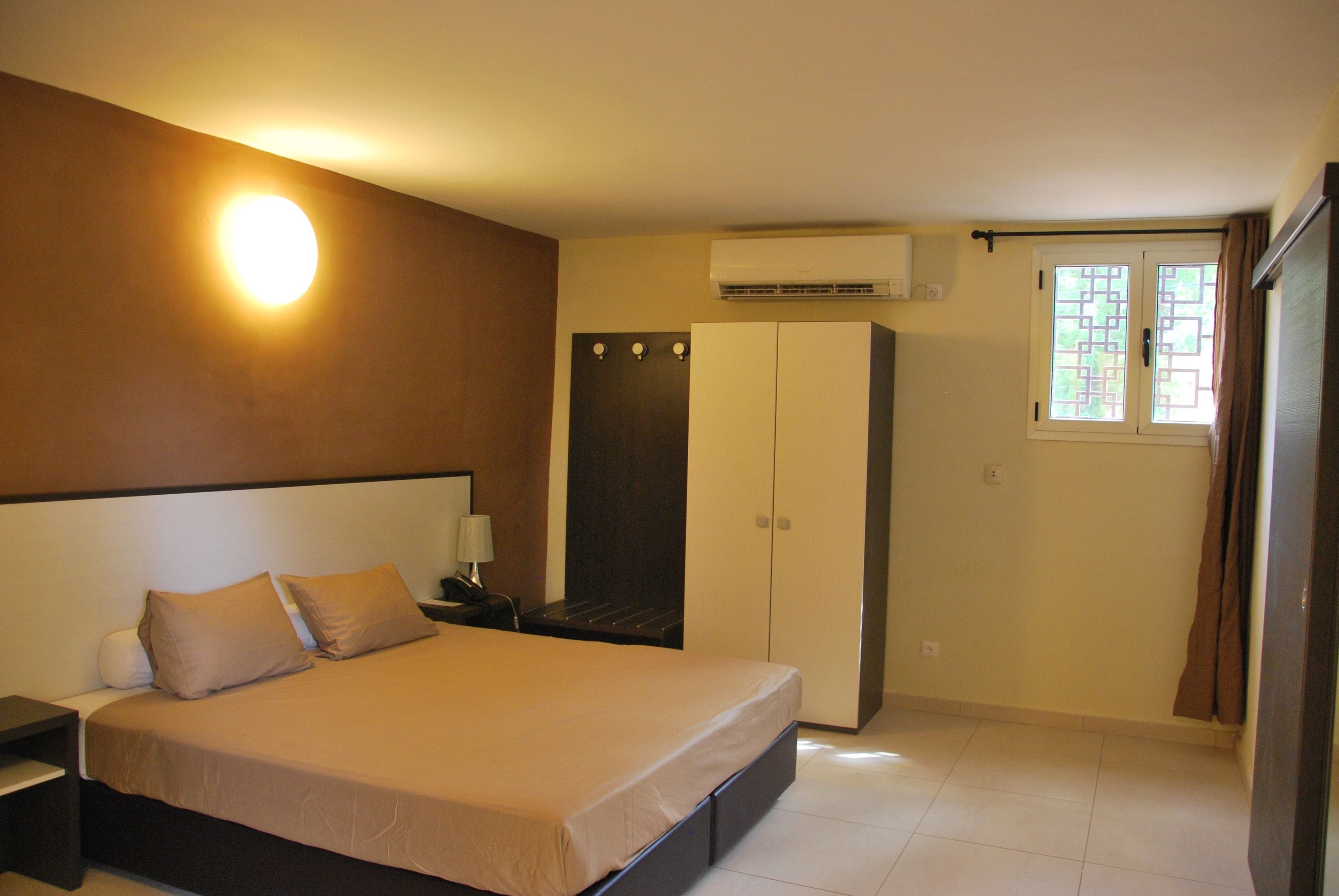 A bedroom with a bed, nightstand, wardrobe, and an air conditioning unit.