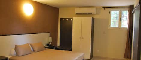 A bedroom with a bed, nightstand, wardrobe, and an air conditioning unit.