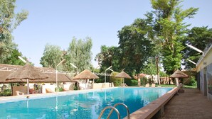 Une piscine entourée d’arbres, agrémentée de chaises longues et de parasols en chaume.