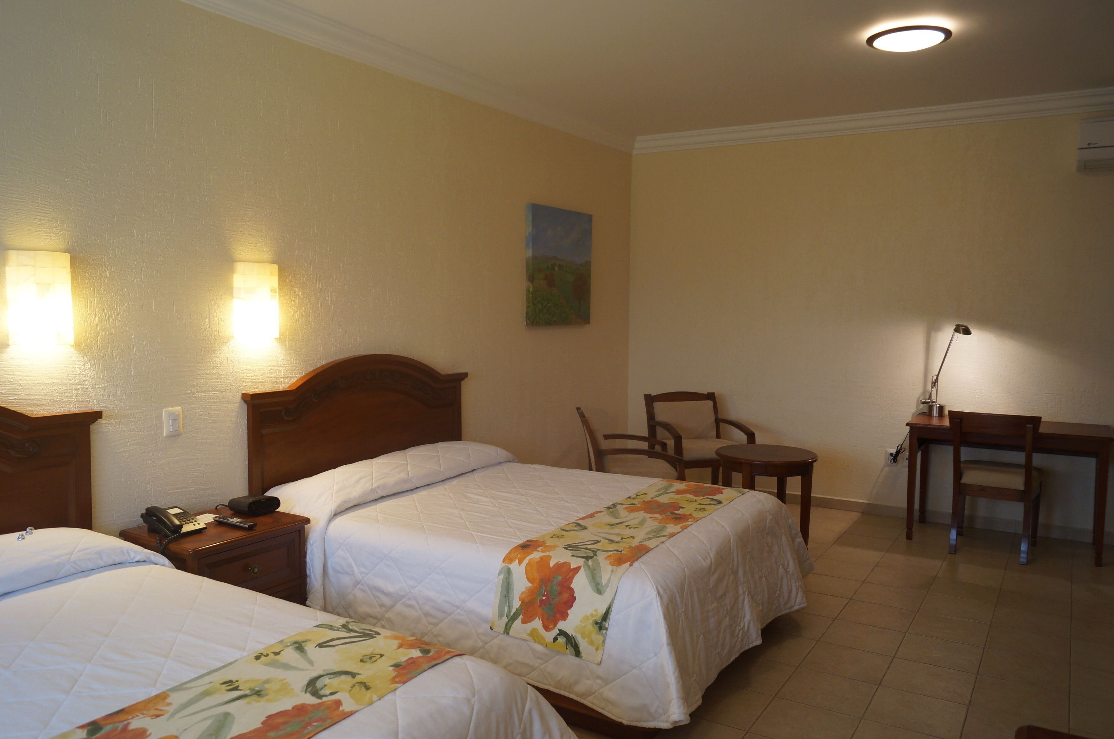 Una habitación de hotel con dos camas, un escritorio, una silla y un cuadro en la pared.