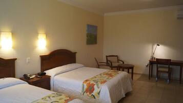 Una habitación de hotel con dos camas, un escritorio, una silla y un cuadro en la pared.