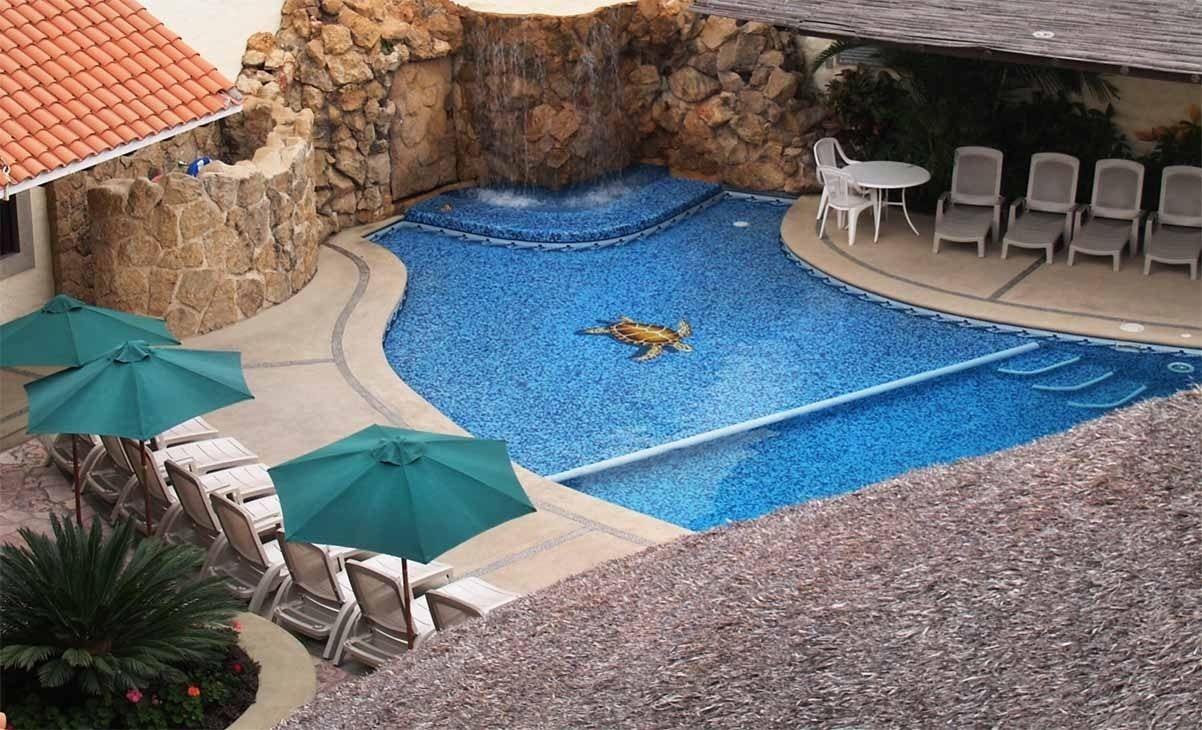 Una piscina con cascada, rodeada de sillas de descanso y sombrillas.