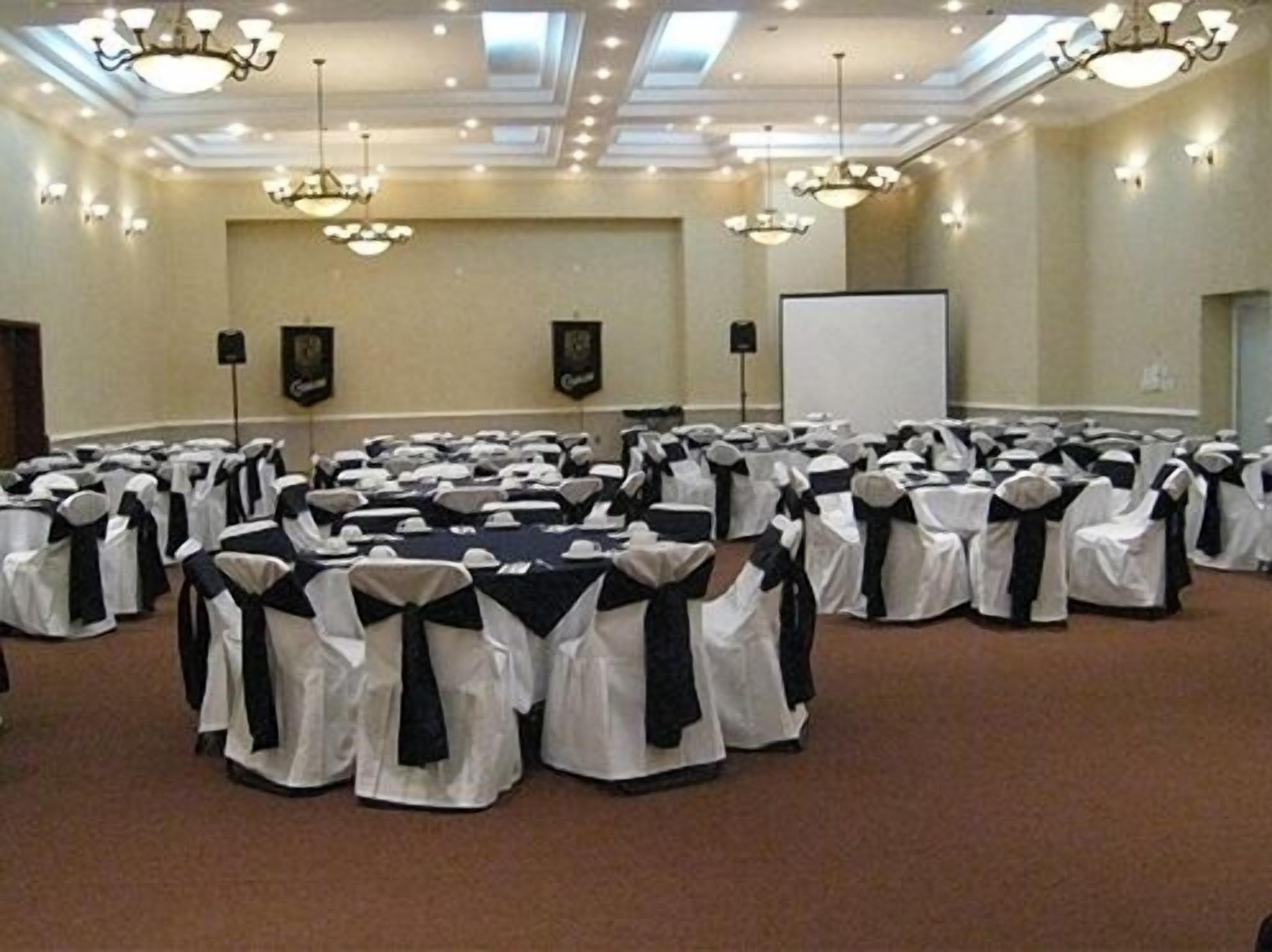 Un salón de conferencias con filas de mesas y sillas, candelabros y una pizarra.