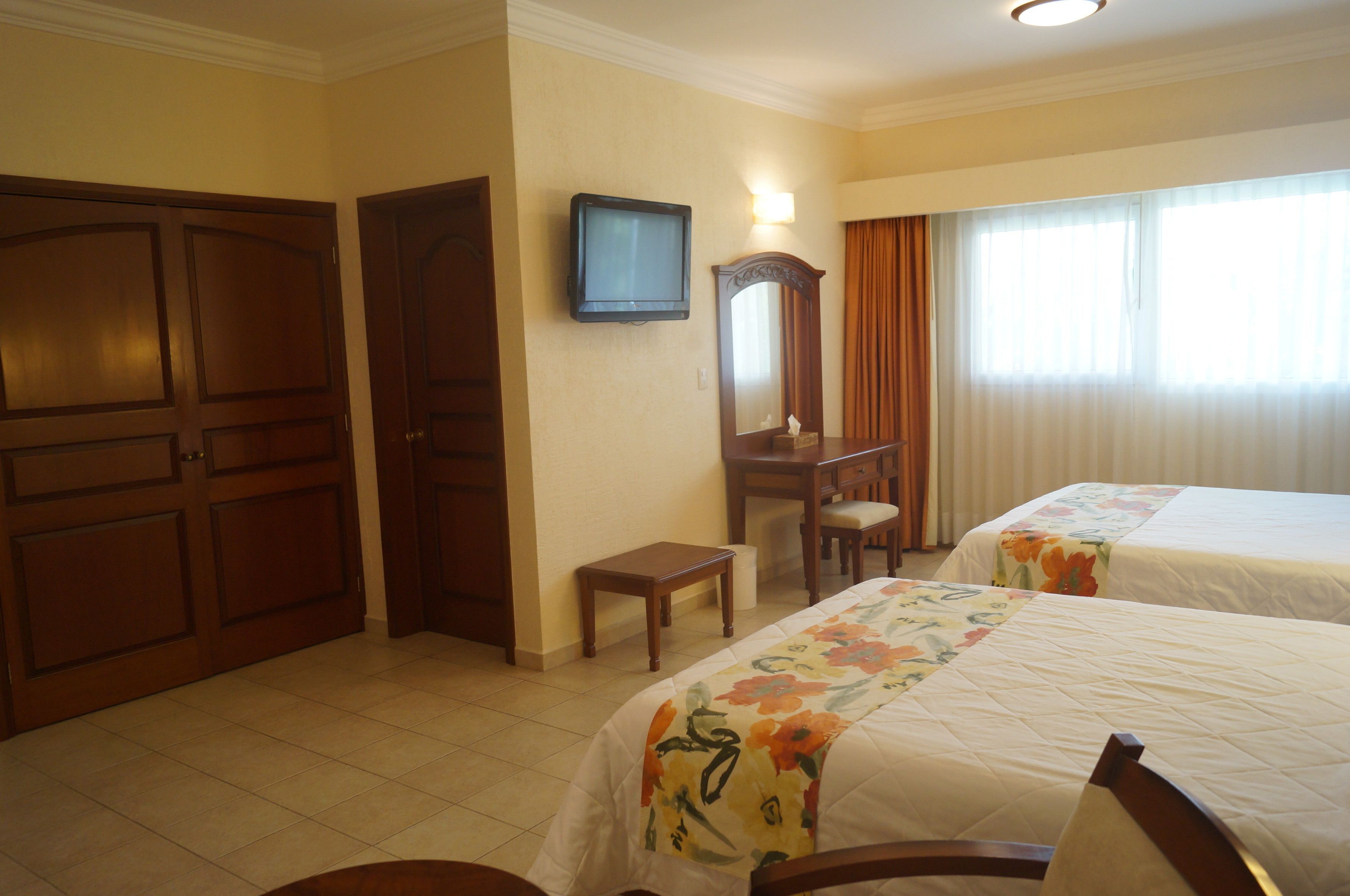 A hotel room with two beds, a television, a desk, and a mirror.