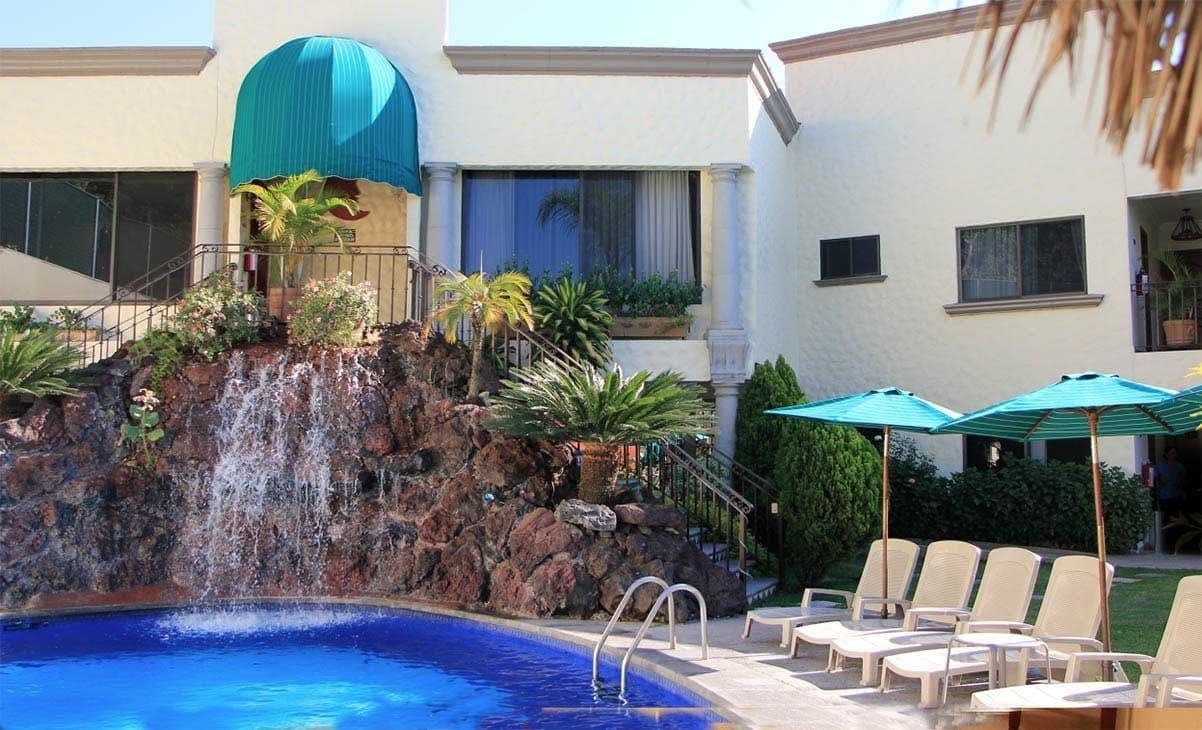A pool area with a waterfall feature, lounge chairs, and umbrellas.