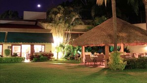 A well-lit outdoor area with a thatched-roof structure, seating, and a building with a green awning. - Hotel Argento (Cuernavaca)