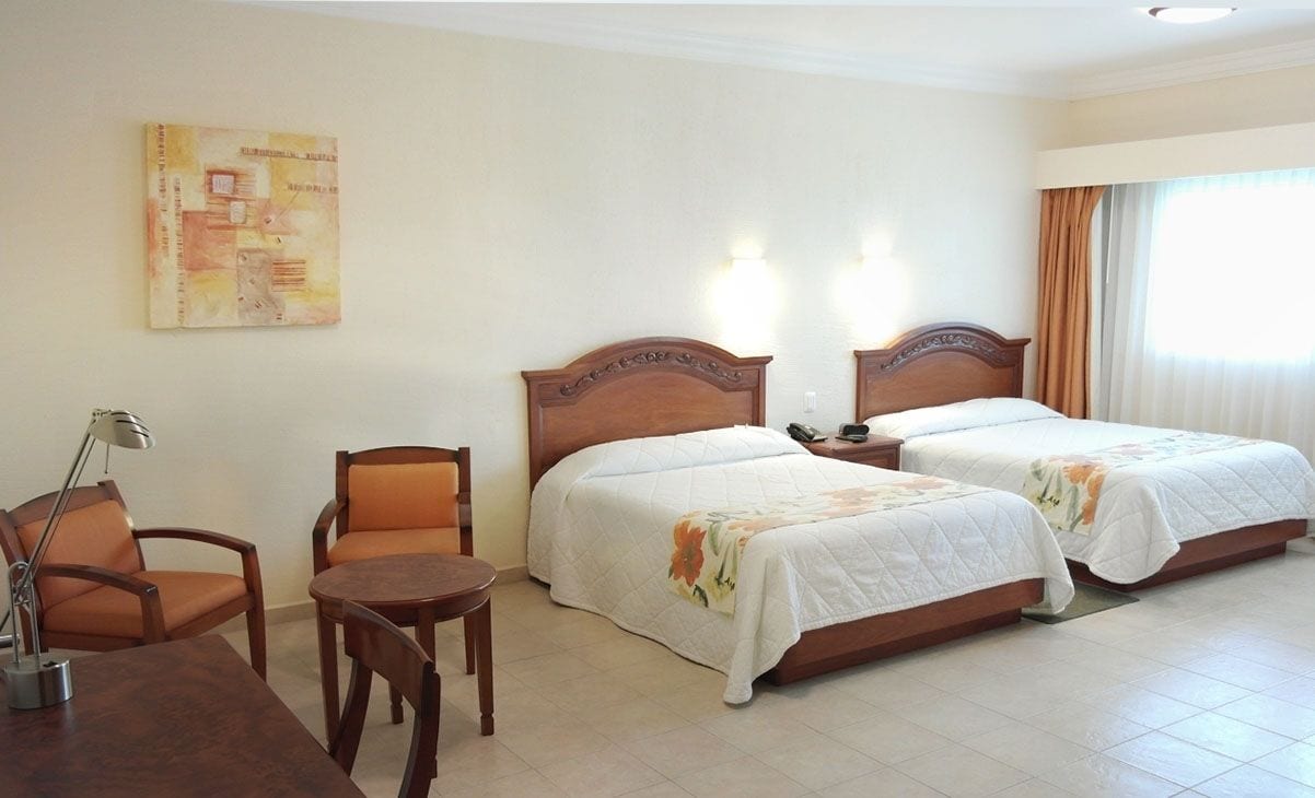 Una habitación de hotel con dos camas, un escritorio, una silla y una lámpara.
