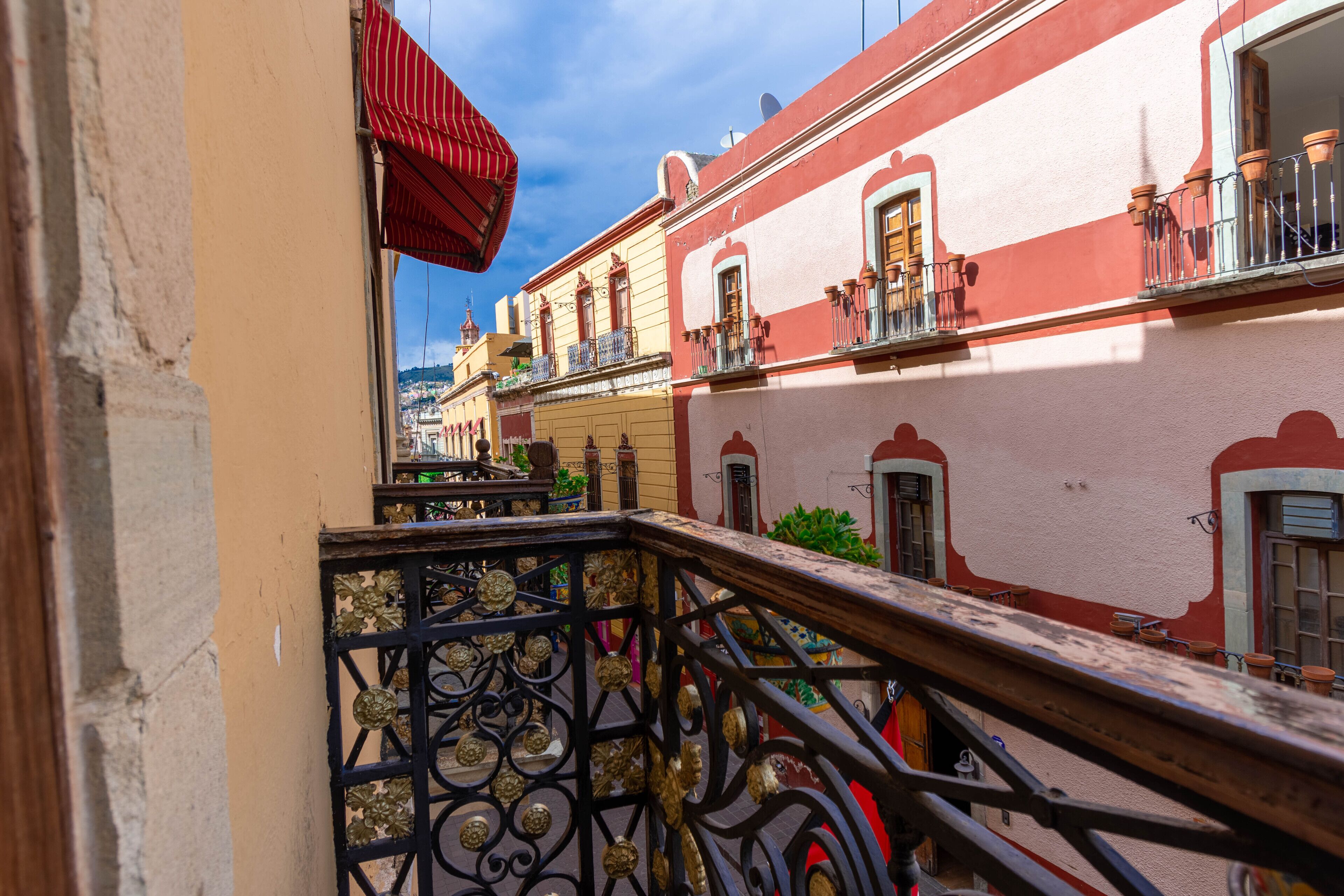 Una calle estrecha flanqueada por edificios, con balcones adornados con plantas en macetas y una barandilla de hierro forjado.